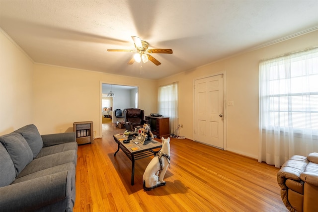 living area with a ceiling fan, heating unit, light wood-style flooring, and crown molding