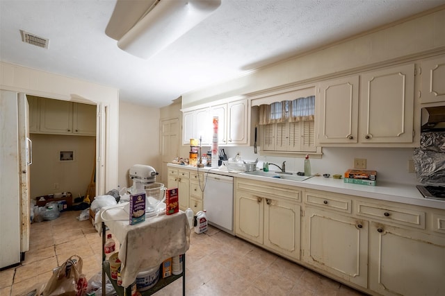 kitchen featuring visible vents, white dishwasher, light countertops, cream cabinetry, and a sink