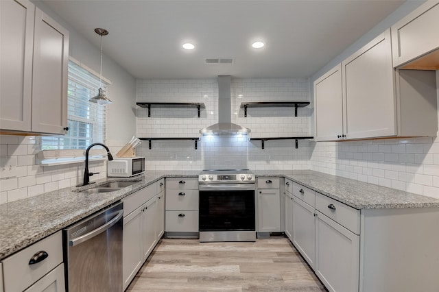 kitchen featuring a sink, appliances with stainless steel finishes, wall chimney range hood, light stone countertops, and open shelves