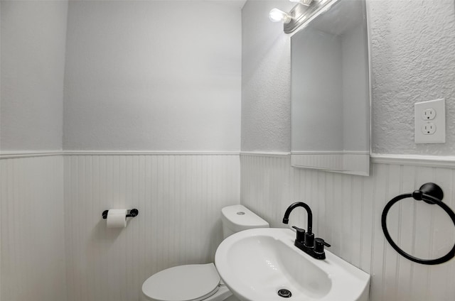 bathroom with a textured wall, a wainscoted wall, a sink, and toilet