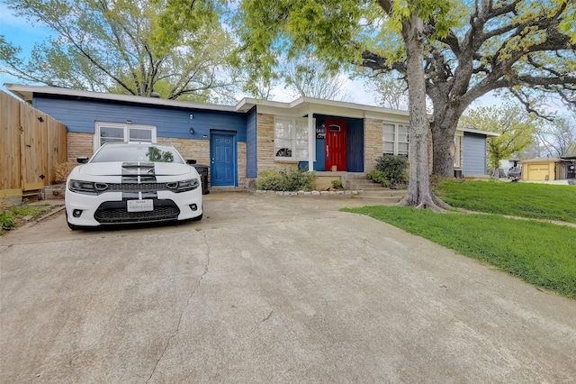 view of front of home with stone siding, a front yard, fence, and driveway