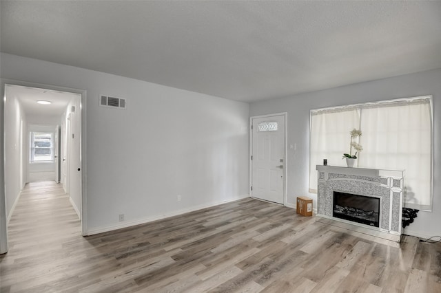 unfurnished living room with a fireplace, wood finished floors, visible vents, and baseboards