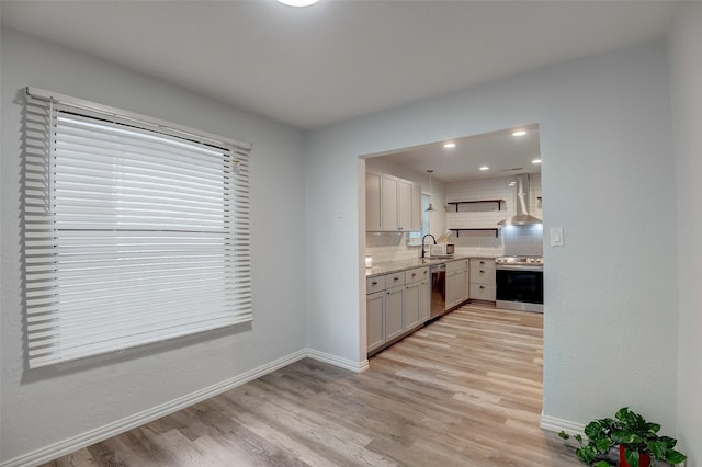 kitchen featuring light wood finished floors, wall chimney exhaust hood, appliances with stainless steel finishes, and decorative backsplash