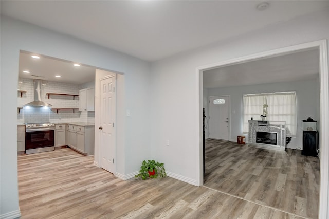 kitchen featuring tasteful backsplash, electric range, light wood-style flooring, wall chimney range hood, and open shelves