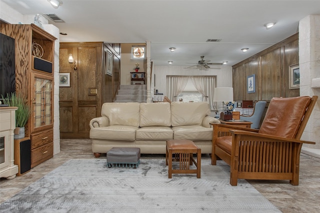 living room with a ceiling fan, visible vents, wooden walls, and stairs