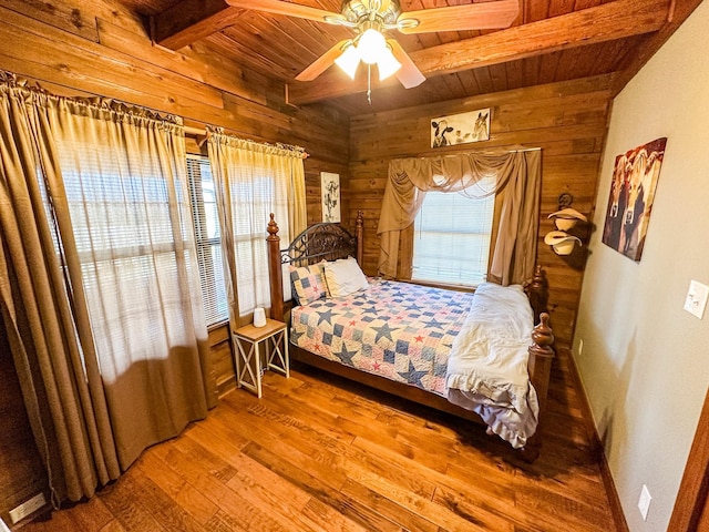 bedroom featuring wooden ceiling, wooden walls, wood finished floors, a ceiling fan, and beamed ceiling