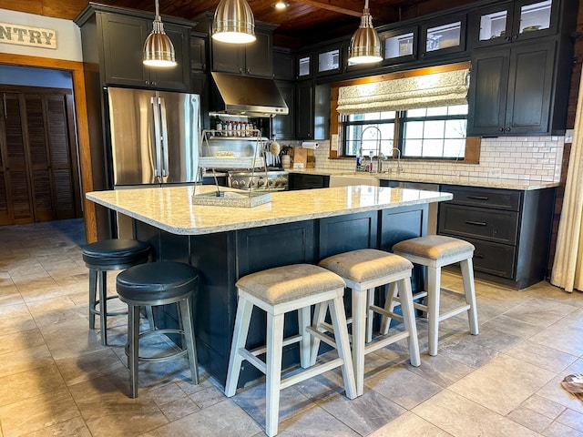 kitchen with light stone countertops, tasteful backsplash, ventilation hood, and freestanding refrigerator