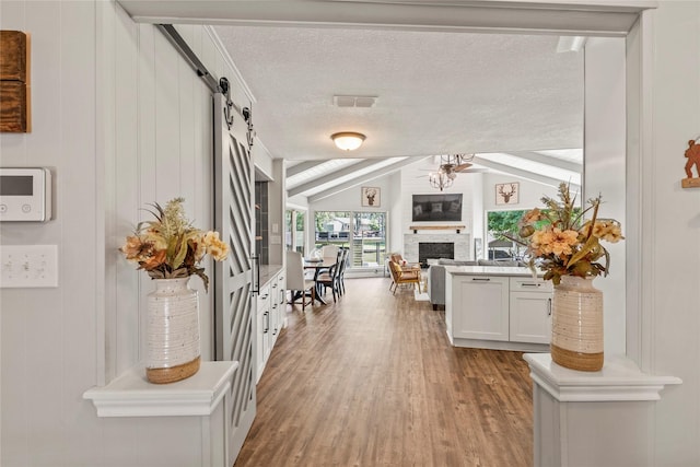 corridor with vaulted ceiling with beams, visible vents, a barn door, a textured ceiling, and wood finished floors