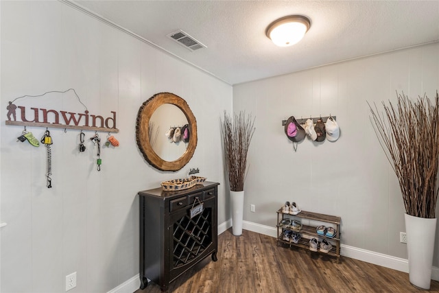 hallway with baseboards, a textured ceiling, visible vents, and wood finished floors