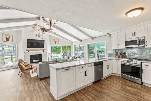 kitchen featuring lofted ceiling with beams, stainless steel appliances, a peninsula, a sink, and white cabinets