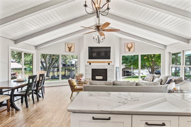 living area featuring vaulted ceiling with beams, plenty of natural light, light wood-type flooring, and a fireplace