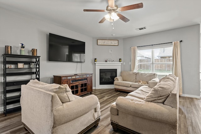 living area with a glass covered fireplace, visible vents, baseboards, and wood finished floors