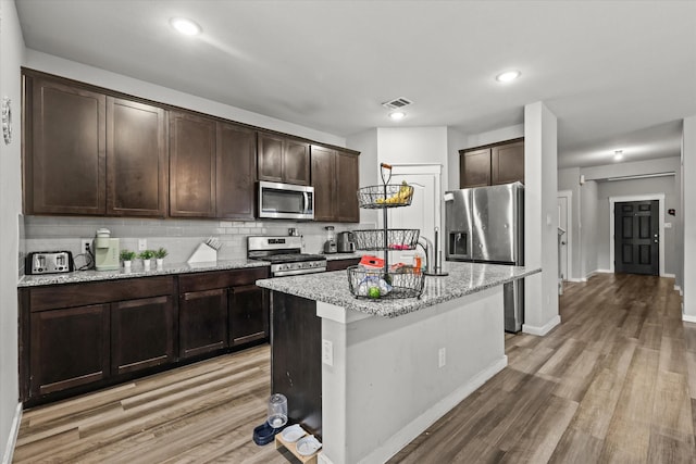 kitchen with dark brown cabinetry, stainless steel appliances, visible vents, light wood finished floors, and tasteful backsplash