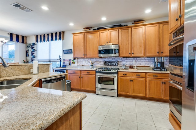 8912 Landmark Ln, Denton, TX 76207 - kitchen featuring stainless steel appliances, a sink, backsplash, light stone counters, and brown cabinets