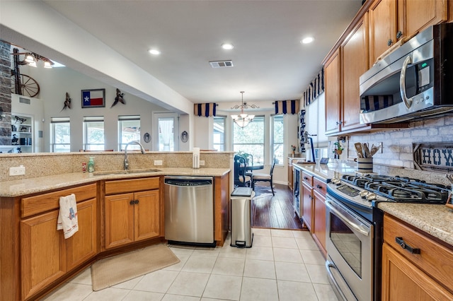 8912 Landmark Ln, Denton, TX 76207 - kitchen with stainless steel appliances, a sink, a chandelier, tasteful backsplash, and brown cabinets