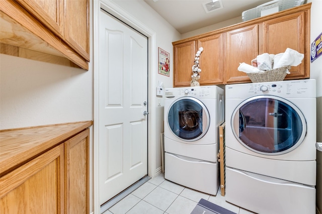 laundry area featuring light tile patterned floors, washing machine and dryer, cabinet space, and visible vents