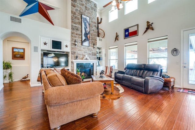 living room featuring visible vents, ceiling fan, a stone fireplace, arched walkways, and wood-type flooring