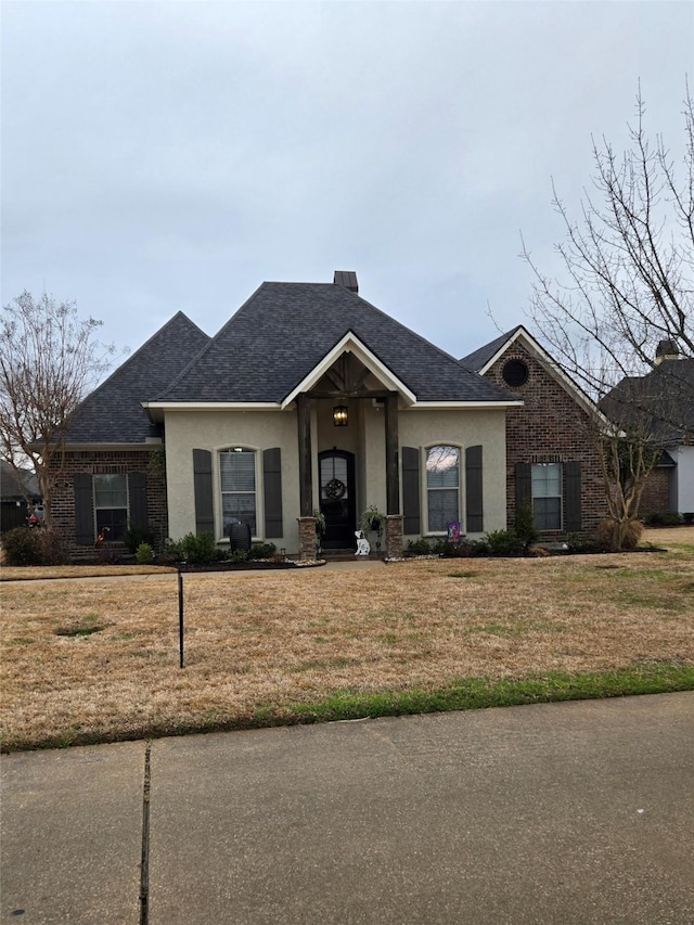 view of front of house featuring stucco siding, a shingled roof, a front yard, and brick siding