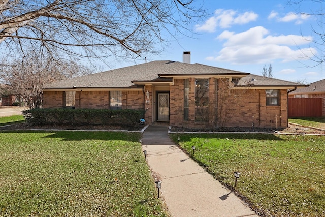 view of front of home with brick siding, a shingled roof, fence, a chimney, and a front yard