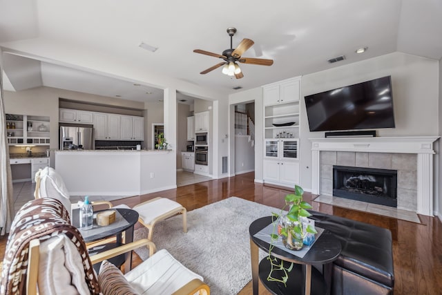 living area with lofted ceiling, a fireplace, wood finished floors, visible vents, and a ceiling fan