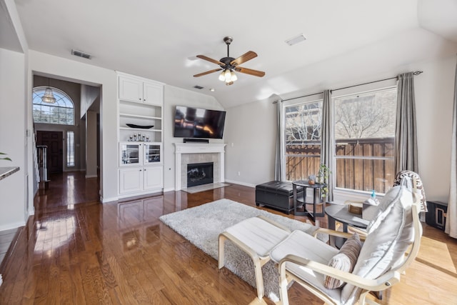 living area featuring visible vents, a tiled fireplace, vaulted ceiling, wood finished floors, and baseboards