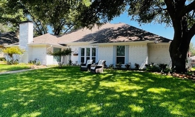 single story home with a front lawn, a chimney, and brick siding