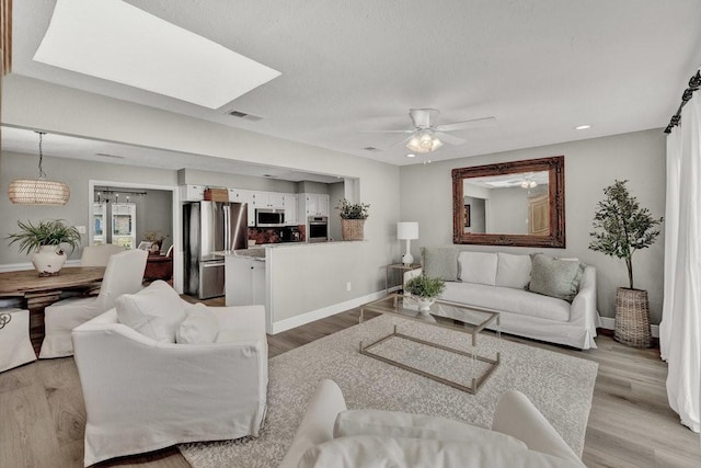 living area with light wood finished floors, ceiling fan, visible vents, and baseboards