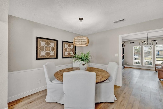 dining room with a textured ceiling, light wood-type flooring, visible vents, and a notable chandelier