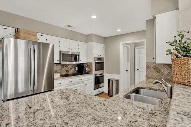 kitchen featuring light stone counters, stainless steel appliances, a sink, white cabinets, and backsplash