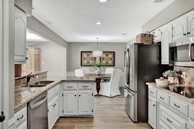 kitchen featuring light wood finished floors, appliances with stainless steel finishes, white cabinetry, a sink, and a peninsula