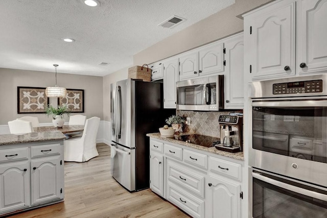 kitchen with appliances with stainless steel finishes, light wood-style flooring, white cabinetry, and decorative light fixtures