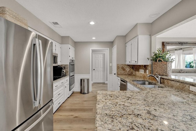 kitchen featuring appliances with stainless steel finishes, light stone countertops, light wood-style floors, white cabinetry, and a sink