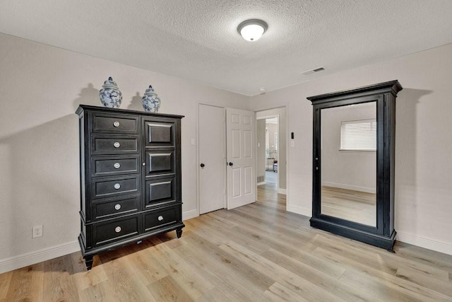 bedroom with a textured ceiling, baseboards, visible vents, and light wood-style floors