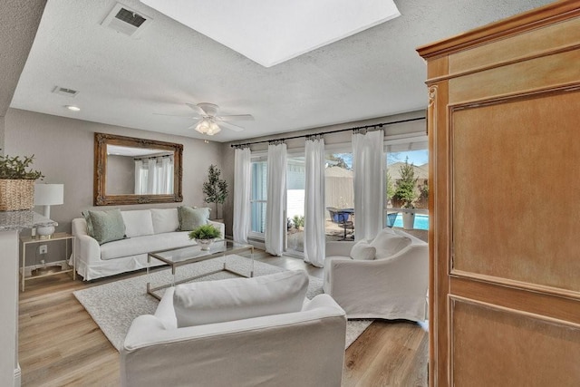 living area featuring light wood-style floors, visible vents, ceiling fan, and a textured ceiling