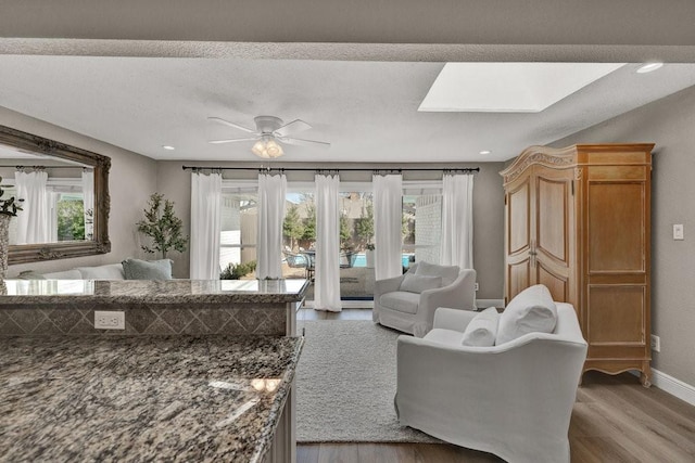 living room featuring a skylight, recessed lighting, light wood-style flooring, ceiling fan, and baseboards