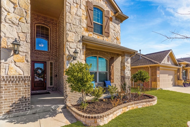 view of exterior entry featuring driveway, a garage, stone siding, a yard, and brick siding