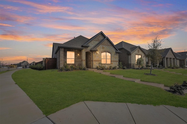 french country inspired facade featuring stone siding, a lawn, and concrete driveway