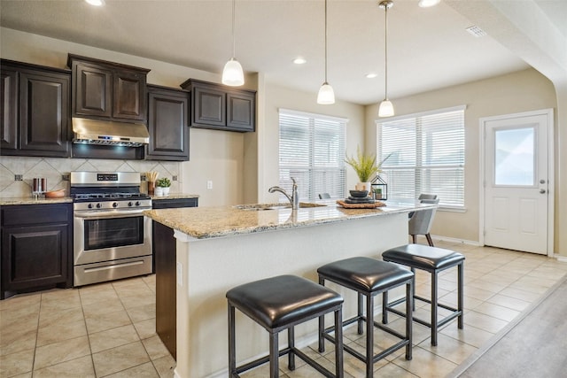 kitchen with light tile patterned floors, gas range, a sink, under cabinet range hood, and backsplash