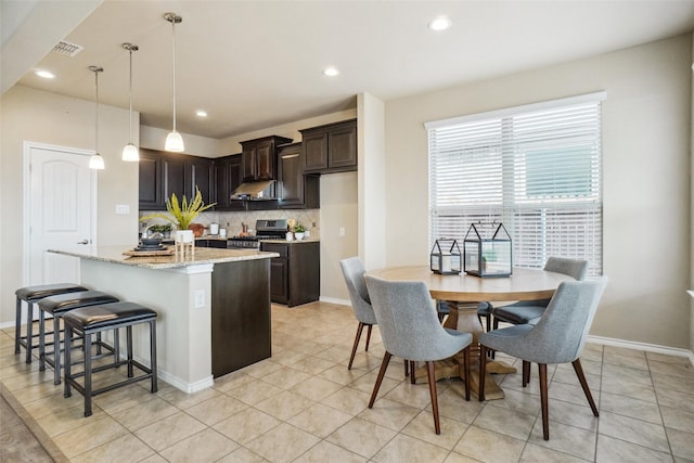 kitchen with a kitchen island with sink, dark brown cabinets, hanging light fixtures, decorative backsplash, and stainless steel gas stove