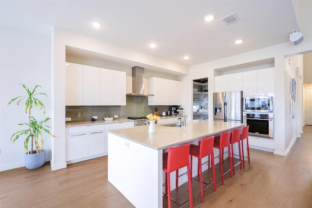 kitchen featuring visible vents, a kitchen bar, appliances with stainless steel finishes, wall chimney exhaust hood, and a sink