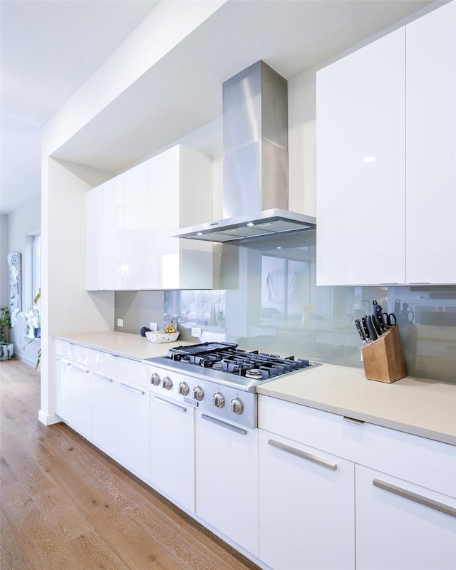 kitchen with light wood-style flooring, wall chimney range hood, backsplash, stainless steel gas stovetop, and light countertops