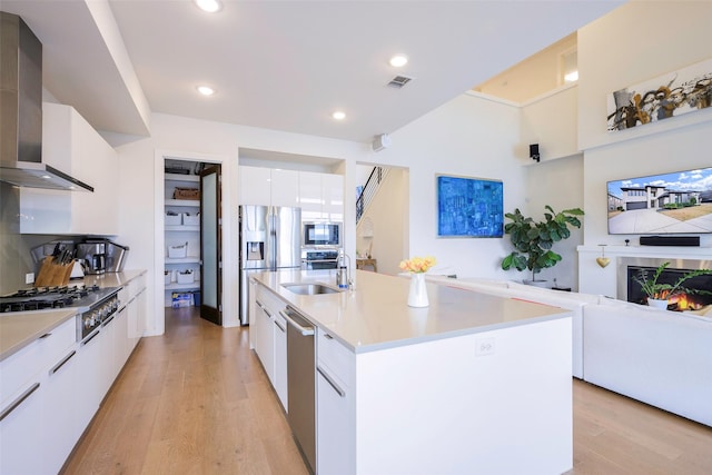 kitchen featuring visible vents, light wood-style flooring, stainless steel appliances, wall chimney exhaust hood, and modern cabinets