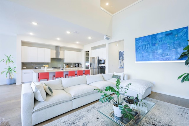 living room with visible vents, baseboards, light wood finished floors, recessed lighting, and a towering ceiling