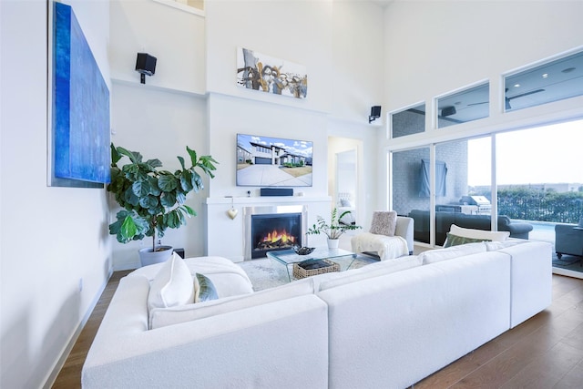 living room with baseboards, a lit fireplace, a towering ceiling, and dark wood-style flooring