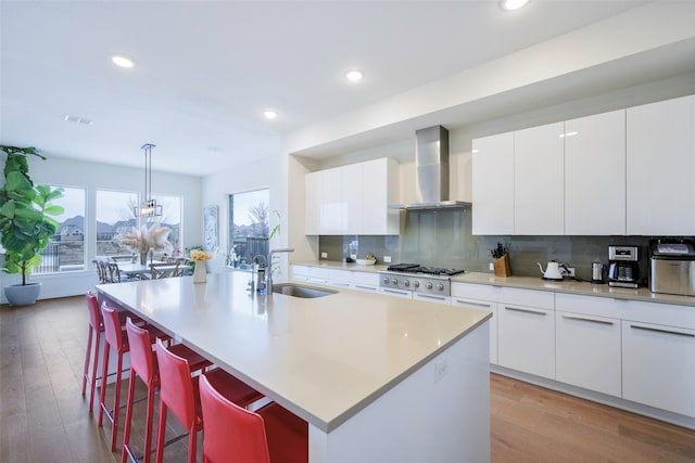 kitchen with stainless steel gas cooktop, a sink, wall chimney range hood, light wood-type flooring, and backsplash