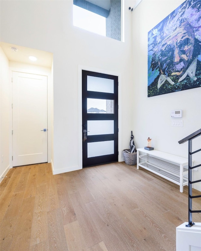 foyer featuring baseboards, a towering ceiling, and wood finished floors