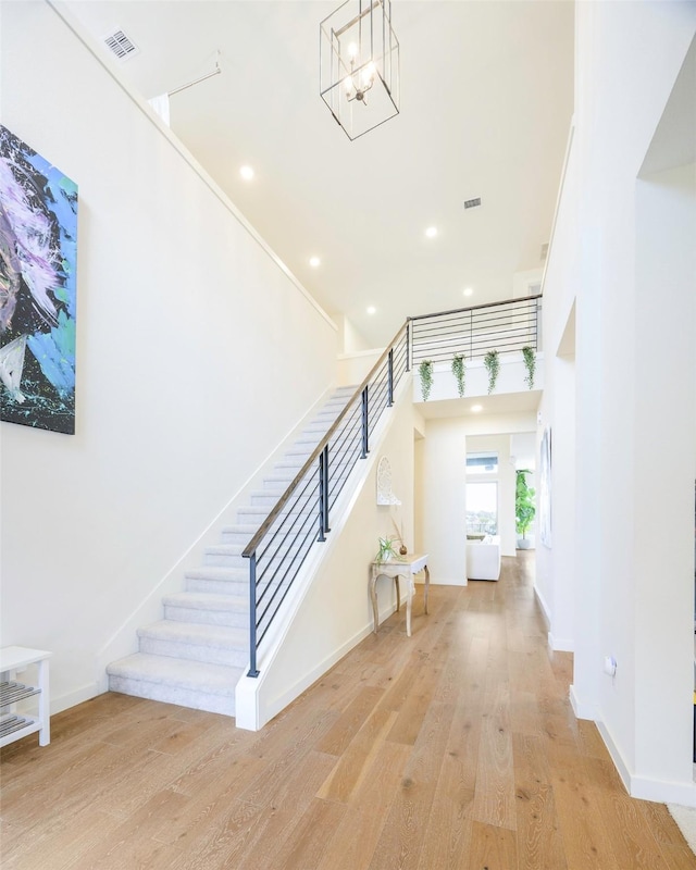 staircase featuring visible vents, baseboards, a high ceiling, an inviting chandelier, and wood finished floors