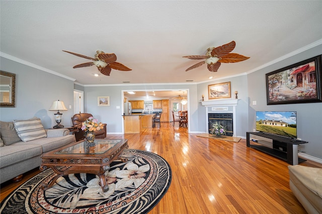 living room with a fireplace, light wood finished floors, ornamental molding, a ceiling fan, and baseboards