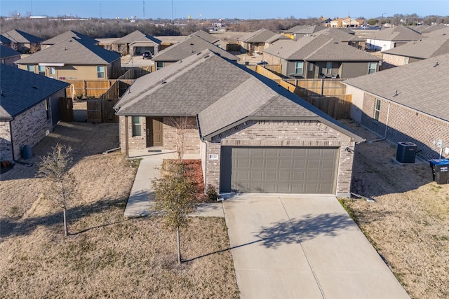 view of front of house featuring brick siding, concrete driveway, central AC unit, fence, and a residential view