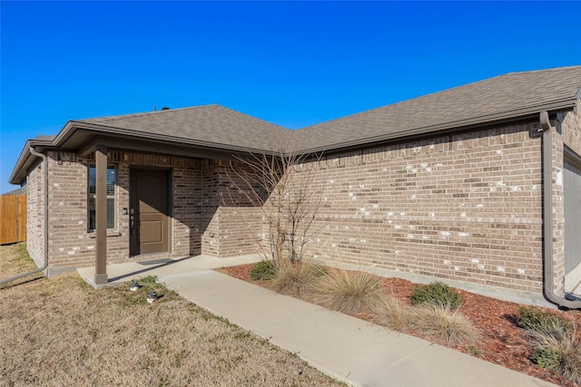 view of exterior entry with brick siding and roof with shingles